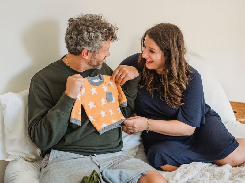 An expecting couple smiling at a tiny baby outfit
