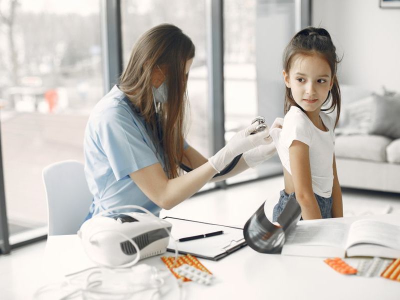 A pediatrician examining a smiling girl in a bright clinic